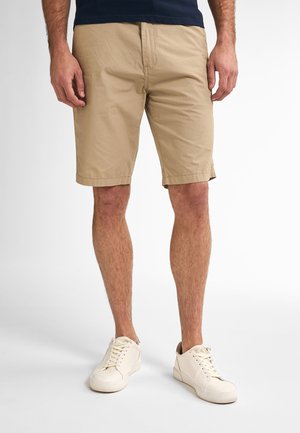 Beige shorts made of cotton with a flat front design, knee-length cut, and subtle side pockets, paired with white sneakers.