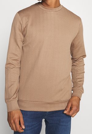 Sudadera beige de manga larga con patrón de espiga texturizado y cuello redondo, combinada con jeans azules.