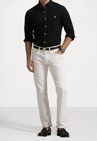 Černá košile na knoflíky, bílé džíny s rovnými nohavicemi, černý opasek se stříbrnou sponou a černé společenské boty. Jednoduchý, čistý design bez vzorů.