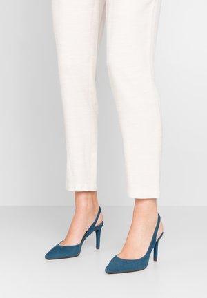 Blågrønne ruskindssko med høj hæl og slingback, med spids tå, slank hæl og åben ryg, kombineret med lyse, taperede bukser.