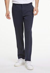 Pantalones azul marino hechos de una tela texturizada, con un diseño de pierna recta, bolsillos laterales y combinados con zapatillas blancas.