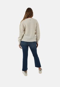 Maglione lavorato a maglia color crema con vestibilità rilassata, abbinato a jeans svasati blu scuro e scarpe platform di colore chiaro.