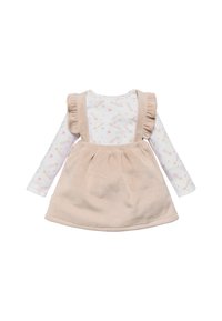 Vestido de tirantes de pana beige con tirantes acampanados sobre una camiseta de manga larga blanca con un patrón de estrellas rosas y amarillas y estrellas fugaces.