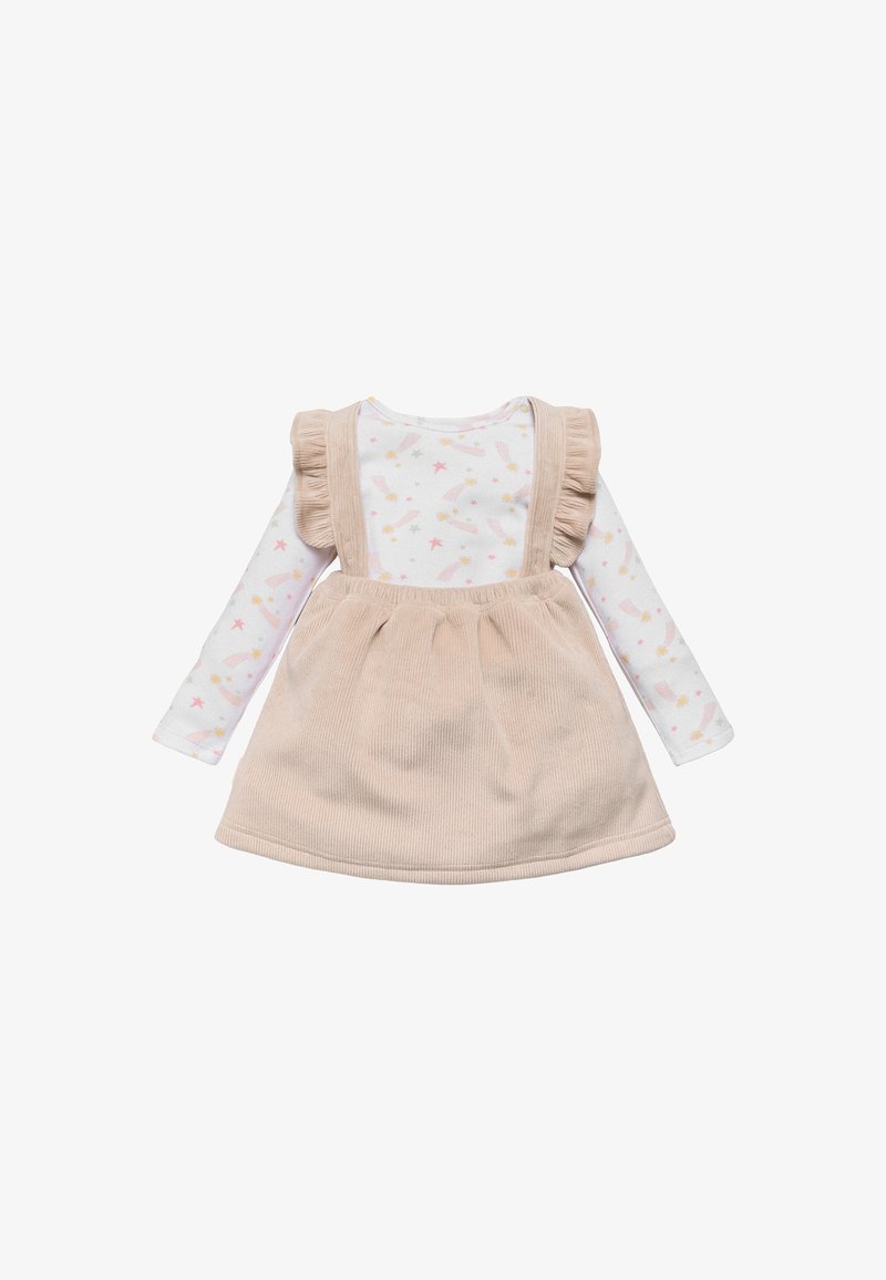 Vestido de tirantes de pana beige con tirantes acampanados sobre una camiseta de manga larga blanca con un patrón de estrellas rosas y amarillas y estrellas fugaces.