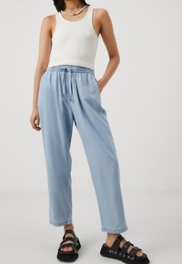 Ljust blå, löst sittande byxor med dragsko i midjan och uppvikta fållar, matchat med en vit ribbad tanktop och svarta sandaletter med remmar.