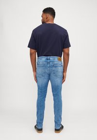 Jeans de mezclilla azul con un corte ajustado y desvanecidos, con bolsillos traseros y un parche de cuero cerca de la cinturilla. Combinados con una camiseta azul marino.