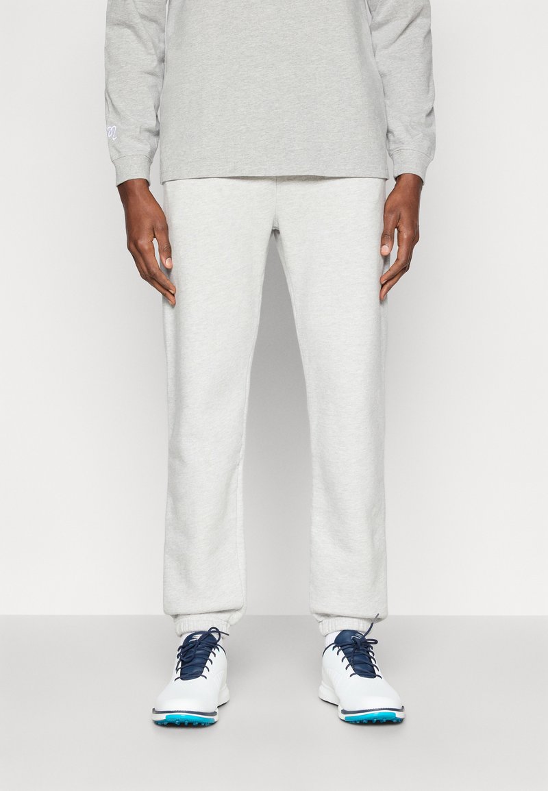 Ανοιχτό γκρι φούτερ και ταιριαστά tapered παντελόνια φόρμας, φτιαγμένα από μαλακό ύφασμα. Διαθέτει ελαστικές μανσέτες και λευκά αθλητικά παπούτσια με μπλε λεπτομέρειες.