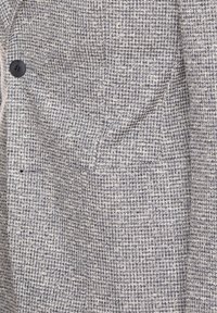 Gewebte Jacke mit strukturiertem Muster in Grau und Weiß, mit einem einzelnen schwarzen Knopf und dezenten vertikalen Linien.