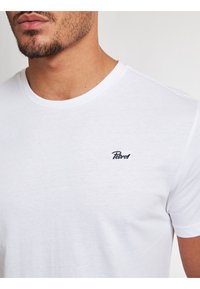 Vit bomullströja med korta ärmar och rund hals, prydd med en liten marinblå "Petrol"-logotyp på vänster bröst.