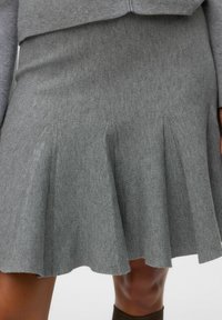 Grå utsvängd kjol av texturerat tyg, med subtila veck och en fåll som mjukt böjer sig. Ren design utan synlig hårdvara.