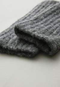 Szary, prążkowany wełniany szalik, złożony w miękki, teksturowany sposób, o ciepłym i puszystym wyglądzie. Widoczne akcenty puszystości w całej powierzchni.