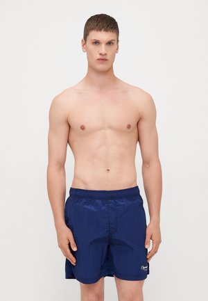 Marineblaue Badeshorts mit elastischem Bund, leichtem Glanz und gesticktem Logo am unteren Saum. Glatt, leicht und mit lockerer Passform.