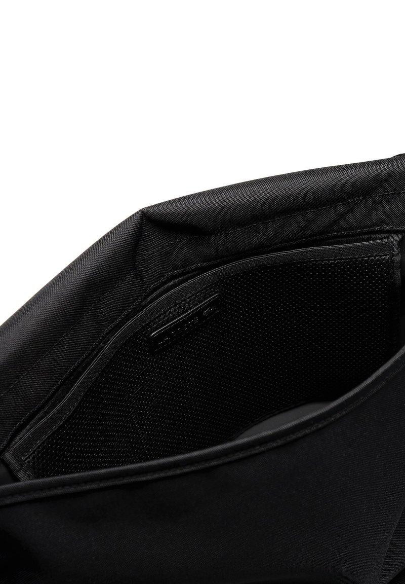 L'intérieur du sac en tissu noir présente une texture lisse, des poches d'organisation et une section en mesh pour le rangement. Une discrète marque est visible.