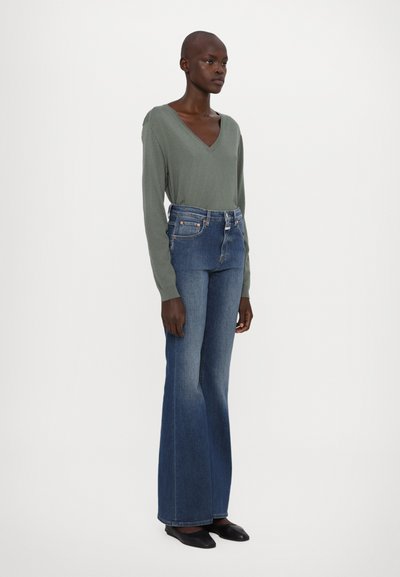Pantalones de mezclilla acampanados de talle alto en denim azul medio, con un ligero desvanecimiento. Complementados con una blusa de manga larga en forma de V de color verde claro.