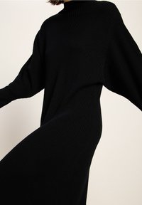 Schwarzes, geripptes Strickkleid mit hohem Kragen und weiten Ärmeln, das eine fließende Silhouette und einen strukturierten Stoff aufweist.