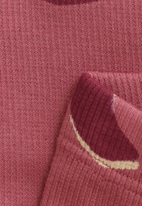 Gros plan d'un poignet de pull en tricot rose plié avec des détails de rayures rose foncé et crème sur un fond de tissu texturé.