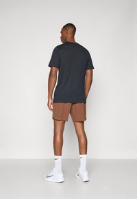 Mørk grå kortermet T-skjorte kombinert med brune shorts, hvite sneakers og anklangshøye sokker, med en avslappet passform og uformell design.