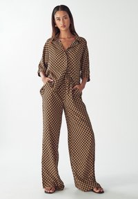 Tan and black patterned two-piece set featuring a loose-fit button-up shirt and wide-leg pants with pockets, made from lightweight fabric.