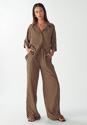 Twee-delige set in een zand- en zwartpatroon, met een losse button-up blouse en brede pantalon met zakken, gemaakt van lichtgewicht stof.