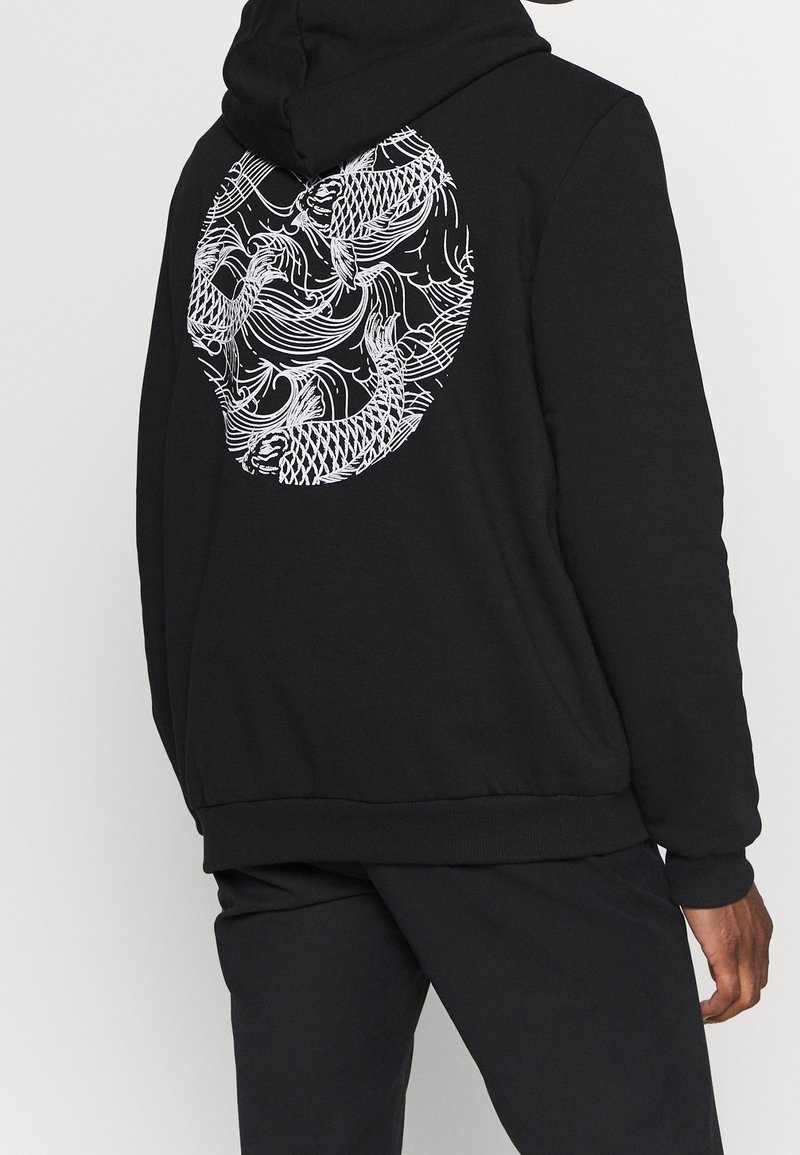 Svart hoodie med en stor vit grafik av fiskar och vågor på baksidan. Mjuk material, avslappnad passform och design med kengurufickor.