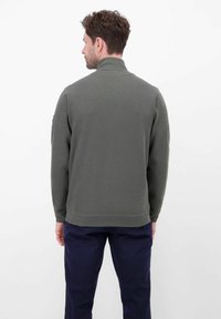 Antracietgroen jack met rits en kraag, van gestructureerde stof, met geribbelde boorden en zoom. Gecombineerd met donkerblauwe broek, gezien van achteren.