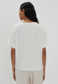 T-shirt blanc à manches courtes avec une coupe décontractée et un col rond. Le tissu semble lisse, léger et se pose à plat contre la peau.
