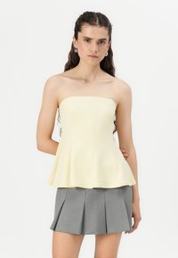 Yellow strapless peplum top in a smooth, stretchy fabric, paired with a pleated gray mini skirt. Simple silhouette without embellishments.