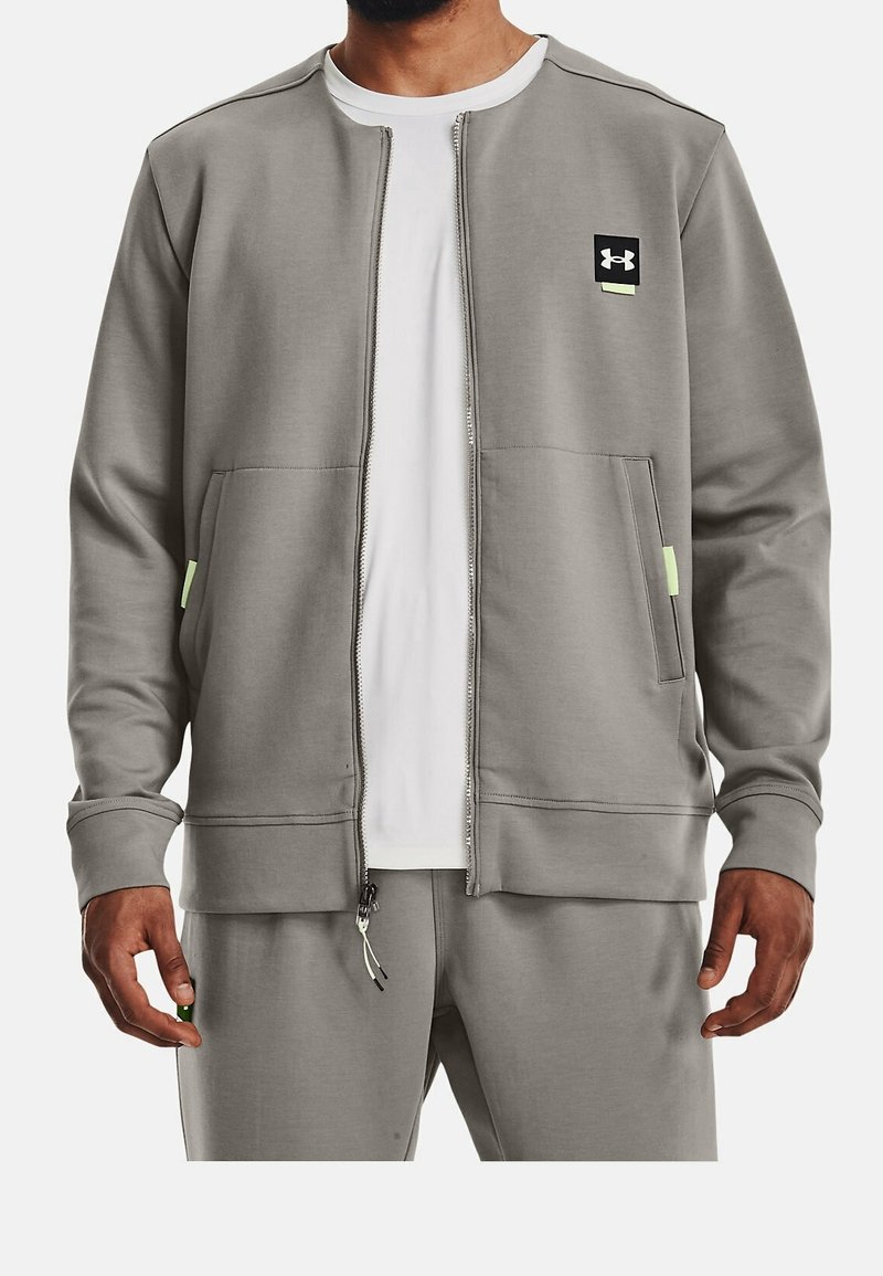 Felpa grigia con zip frontale realizzata in tessuto morbido, con un piccolo logo nero sul petto, due tasche anteriori e dettagli in verde neon.
