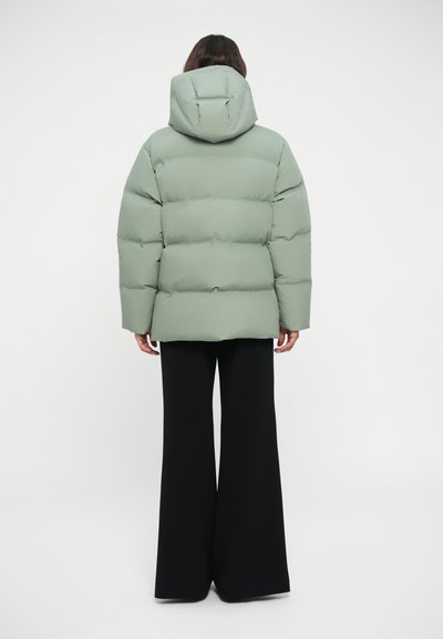 Puffer jacket in light green with a hood, structured with oversized panels and a smooth texture, paired with wide black pants.