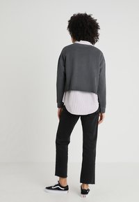 Sudadera gris recortada sobre una camiseta blanca y gris a rayas, combinada con jeans negros y zapatillas negras. Los materiales parecen casuales y cómodos.