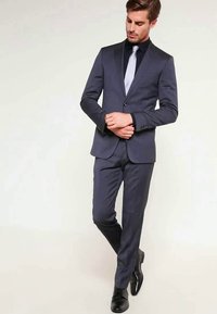 Fato azul-marinho com um design slim fit, apresentando um fecho de um botão, textura mate e uma camisa preta em contraste com uma gravata cinza-clara.