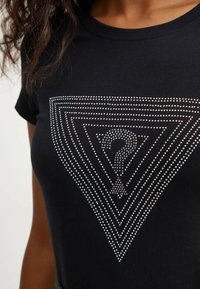 Zwarte t-shirt met een driehoekig ontwerp van zilveren studs, met een vraagtekenmotief in het midden. Glad van textuur.