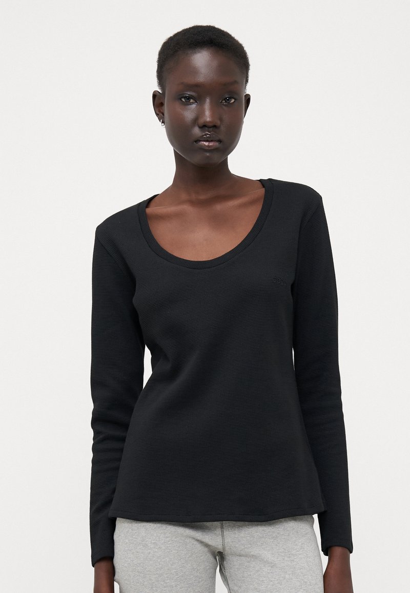 Camisola preta de manga longa com decote em forma de coração e textura canelada. Apresenta uma barra ligeiramente evasé e um pequeno detalhe de logótipo na parte da frente.