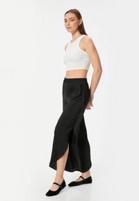 Hvid crop top parret med sorte brede bukser med sideslids, glat tekstur, elastisk talje og sorte flade sko med stropper.