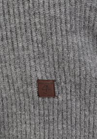 Grijze gebreide stof met een geribbeld patroon en een bruine leren patch met het label "KEY LARGO" in de linkerbovenhoek.