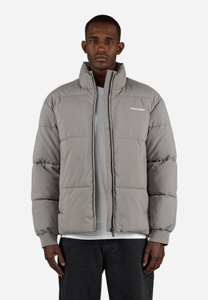 Gray puffer jacket with a high collar, zip closure, and elasticized cuffs. Features stitched panels and logo on the chest. Worn over a light shirt.