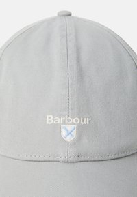 Căciulă de baseball ușor gri, cu "Barbour" brodat în alb deasupra unui scut mic care are un crucifix albastru.