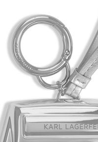 Zilveren metallic tas hardware met een ronde ring en een band met een gestructureerde afwerking. Gegraveerde merknaam zichtbaar.