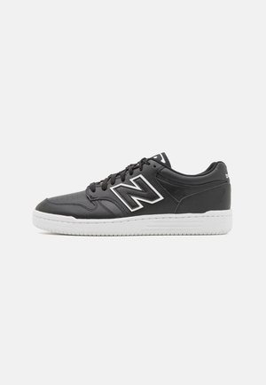 Baskets basses noires avec semelle blanche et grand logo "N" bordé de blanc sur le côté, vues du côté extérieur.
