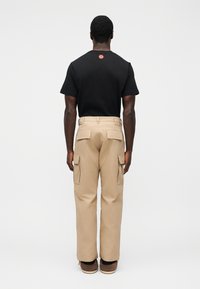 Μαύρο βαμβακερό T-shirt με κόκκινη κυκλική λεπτομέρεια στη ράχη, σε συνδυασμό με μπεζ παντελόνι cargo με πολλές τσέπες και χαλαρή εφαρμογή.