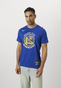 Tricou din bumbac bleu cu logo-ul Golden State Warriors, un design grafic rotund, mâneci scurte și logo-ul Nike pe umărul stâng.
