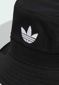 Black bucket hat made of textured fabric with a white embroidered logo featuring three leaves and horizontal stripes.