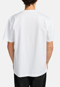 T-shirt bianco in cotone con maniche corte, colletto rotondo e una vestibilità rilassata. La parte posteriore presenta un design pulito, senza loghi o motivi visibili.