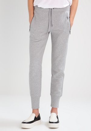 Pantalon jogger slim gris clair avec poches zippées et poignets aux chevilles, porté avec des chaussures slip-on noires et blanches.