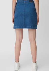Jupe en denim bleue, avec une coupe ajustée, longueur mi-cuisse et poches arrière. Finition avec des coutures visibles et une étiquette sur la taille.