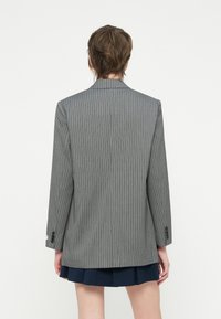 Pelēks pinstripe žakets ar pielāgotu piegriezumu, ar locītavu atvērumiem, garām piedurknēm, vienu pogu pie mutes un gludu auduma tekstūru.