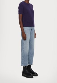 Krátké fialové pletené tričko s kulatým výstřihem, doplněné světle modrými širokými džínami a černými robustními kotníkovými botami.