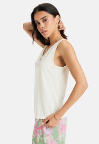 Lichtbeige tanktop met een relaxte pasvorm, voorzien van een ronde hals en subtiele roze tekstontwerpen, gecombineerd met shorts met bloemenpatroon.