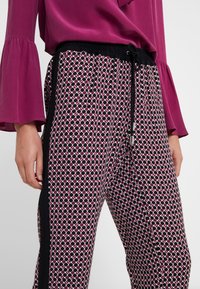 Zwart-wit gestreepte broek met roze accenten, elastische tailleband met trekkoord, zijstreep in het zwart, en een zijdezachte, gladde textuur.