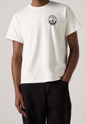 Biała bawełniana koszulka z krótkim rękawem i okrągłym dekoltem, z czarnym okrągłym logo na lewej części klatki piersiowej.